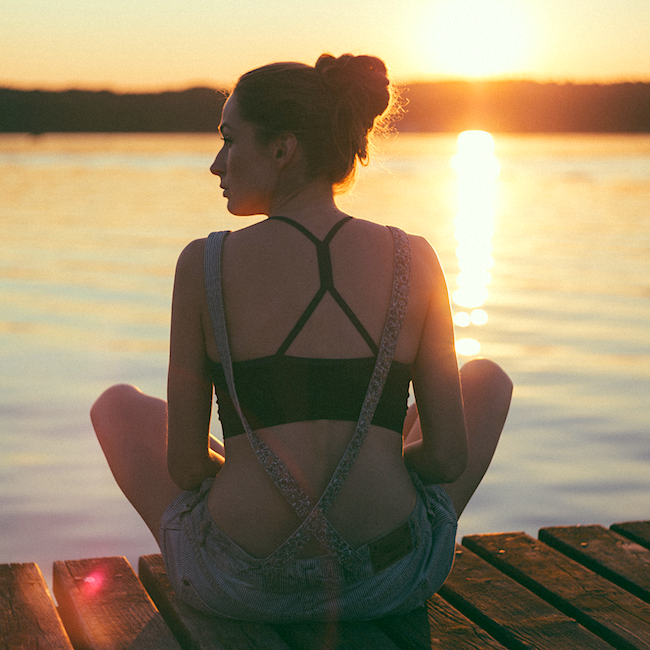 A girl meditates and enjoys the sunset by the water.